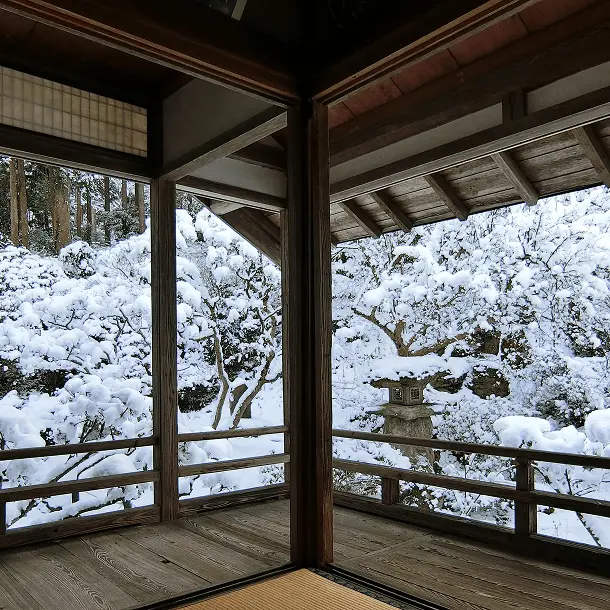 岩松院の縁側から望む雪化粧した庭園、石灯籠と雪に覆われた樹木が織りなす冬の静寂な風景