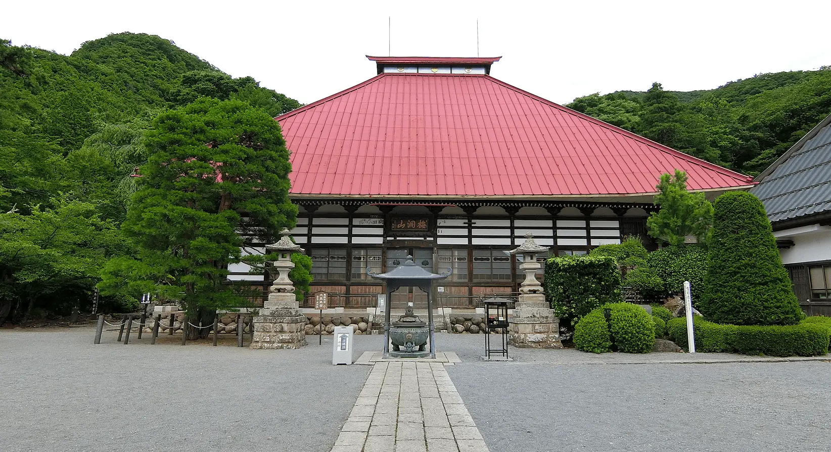 赤い屋根の岩松院本堂と、その前に整えられた植木と石灯籠。夏の緑に映える静かな境内