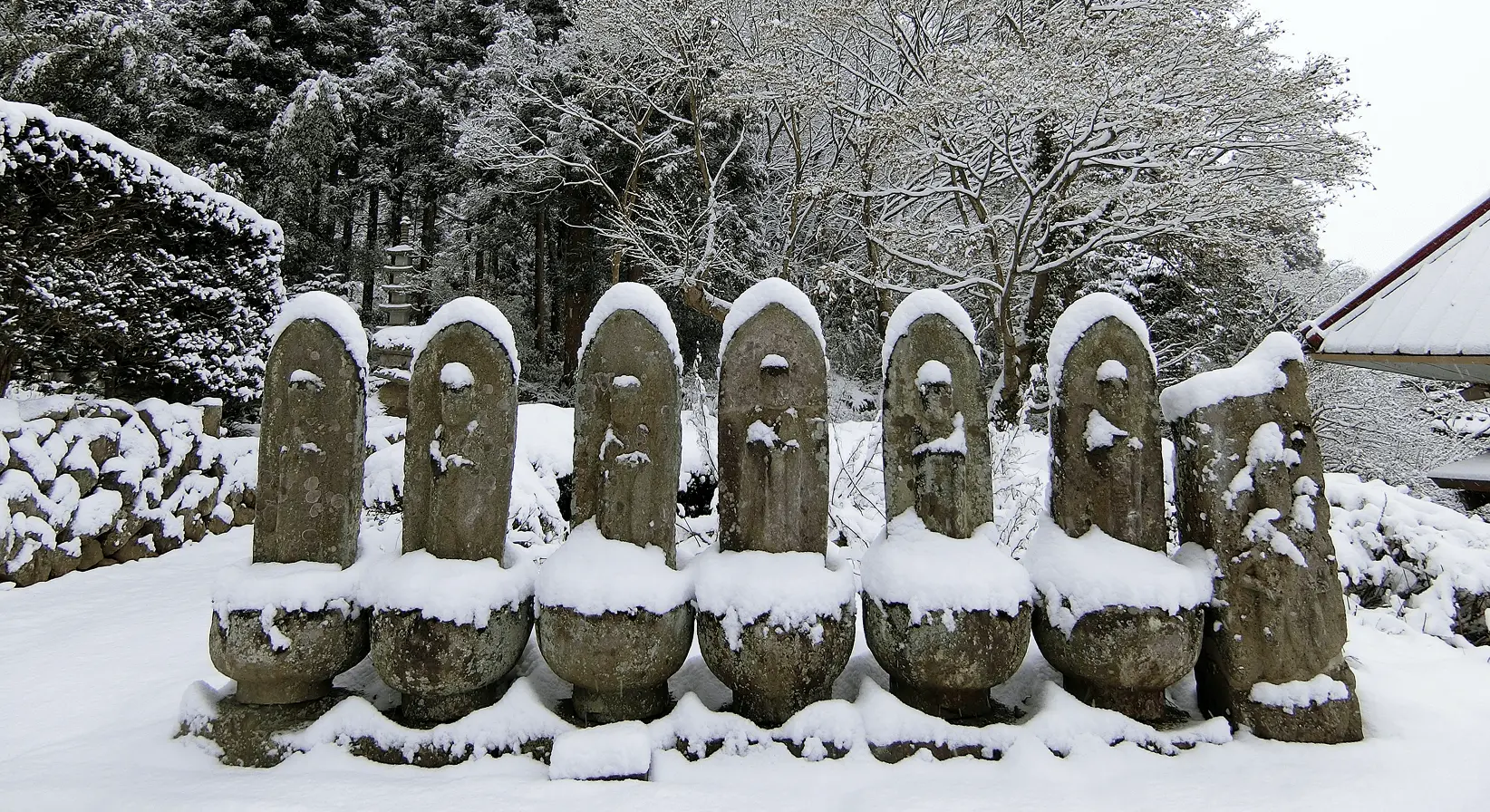 雪をかぶった複数の石仏が並ぶ岩松院の境内。静かで神聖な空気が漂う冬の風景