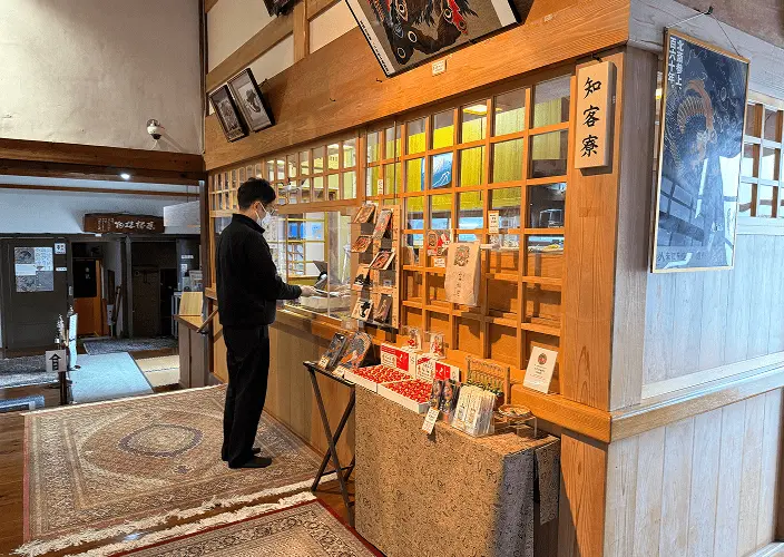 岩松院本堂内の展示・売店エリア、木製の棚に御朱印や書籍が陳列され、参拝者が閲覧している様子